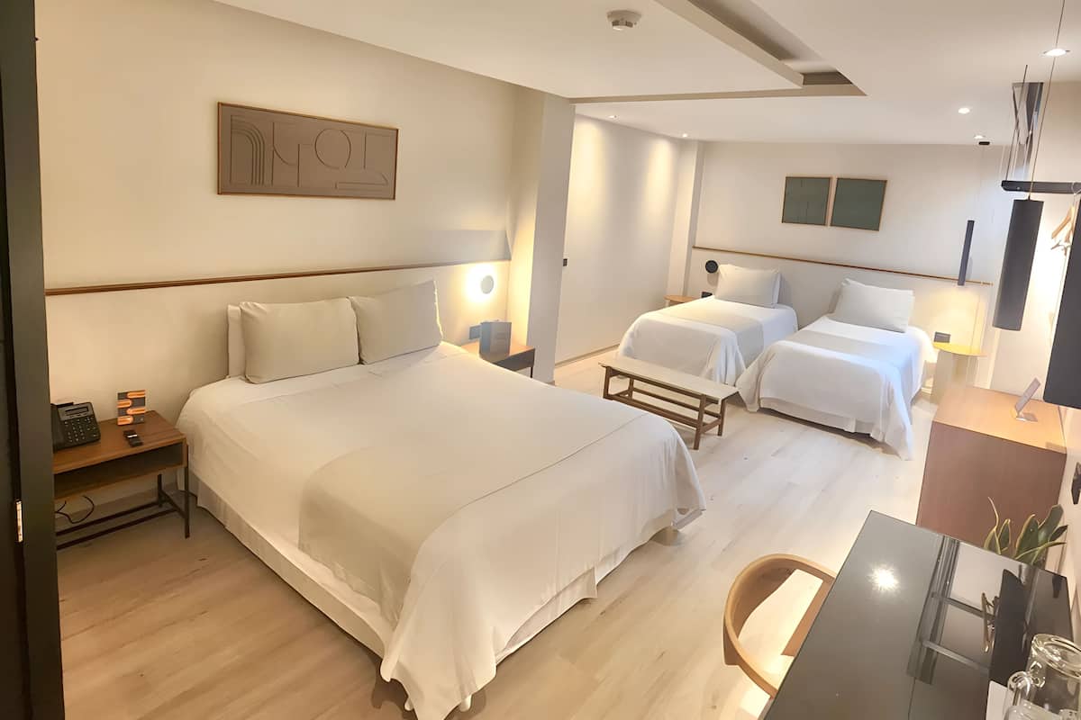 A hotel room with two beds, a desk, and a chair. There is a painting on the wall and a ceiling light.