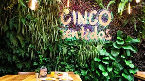 A restaurant interior with a wooden table, chairs, and a wall decorated with green plants and a neon sign reading "CINCO Sentidos". - Hotel Finlandia (Quito)