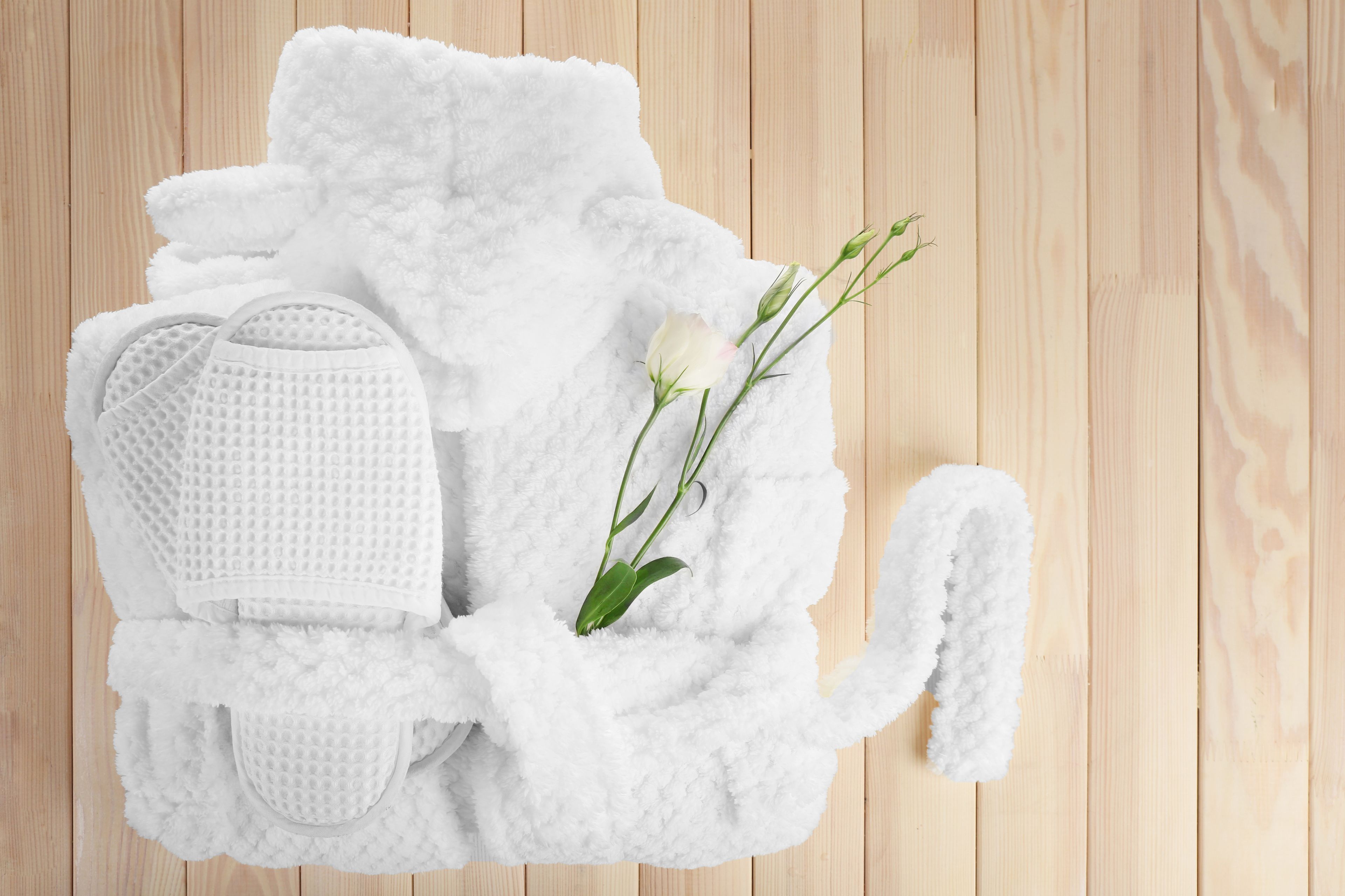 A white bathrobe, slippers, and a rose on a wooden floor.