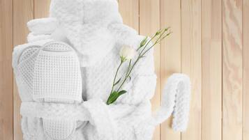 A white bathrobe, slippers, and a rose on a wooden floor.