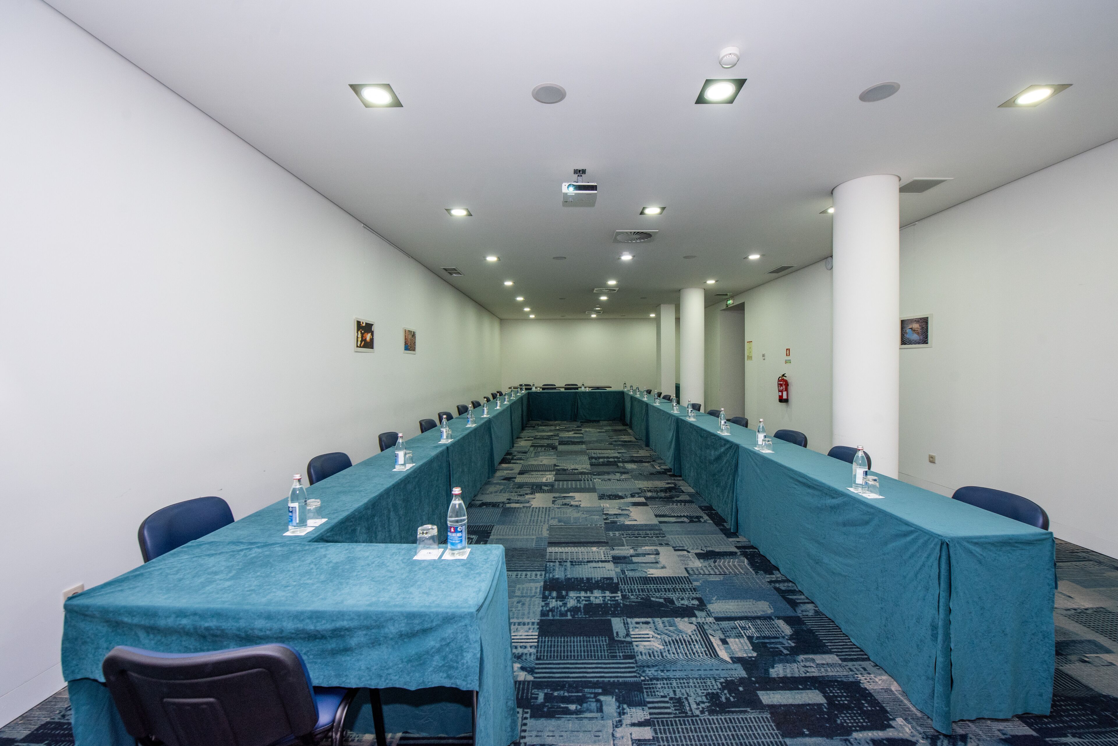 Un salón de conferencias con una larga mesa, sillas y botellas de agua.