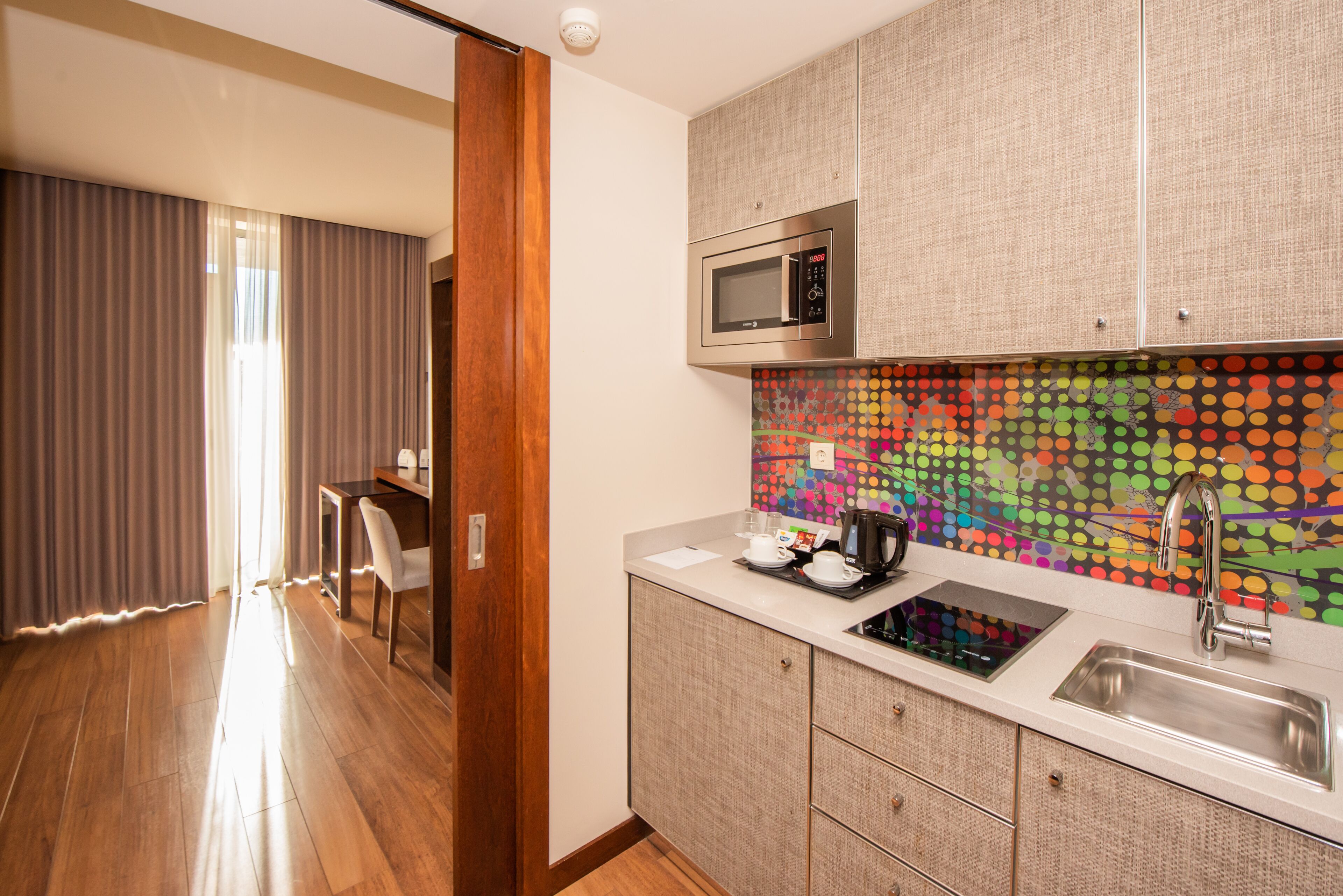 A modern kitchen with a microwave, sink, and a colorful dot-patterned backsplash.