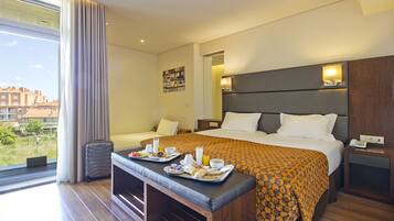 Een hotelkamer met een bed, een bankje met ontbijtplateaus, een koffer en uitzicht op gebouwen.
