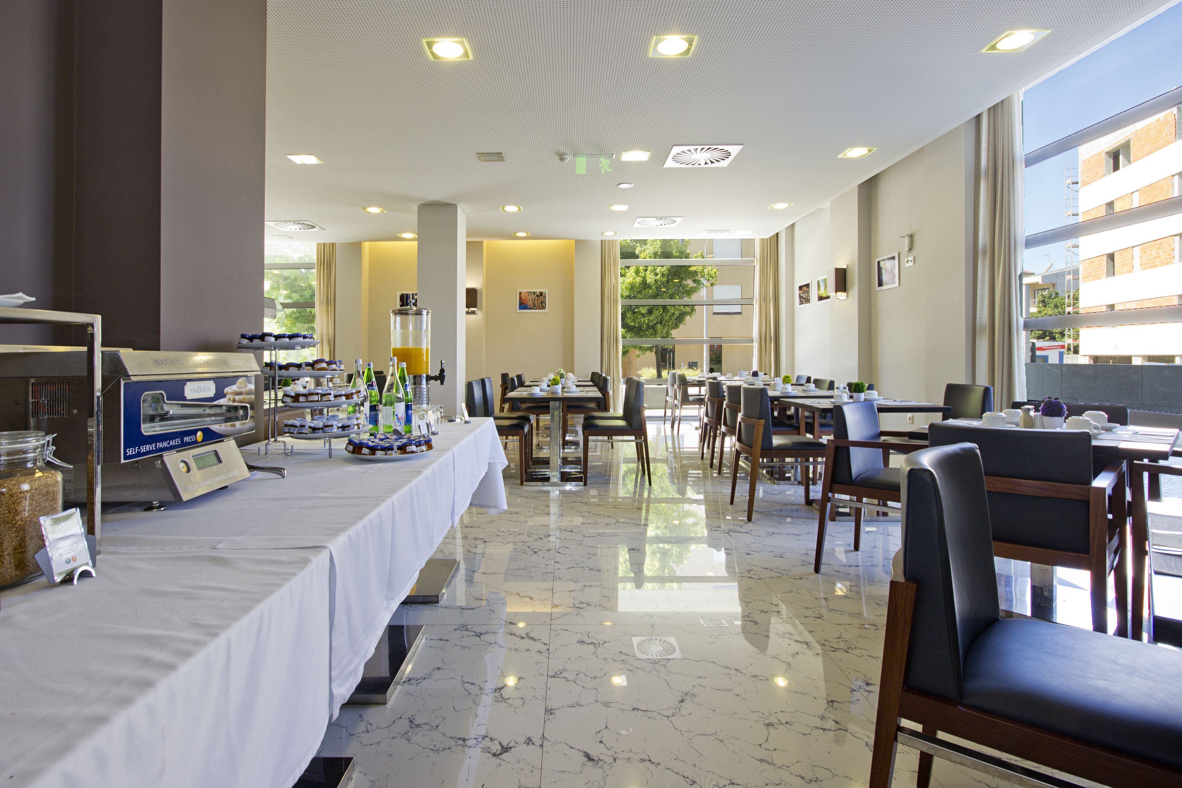 A hotel dining area with a buffet setup, multiple dining tables, and chairs.