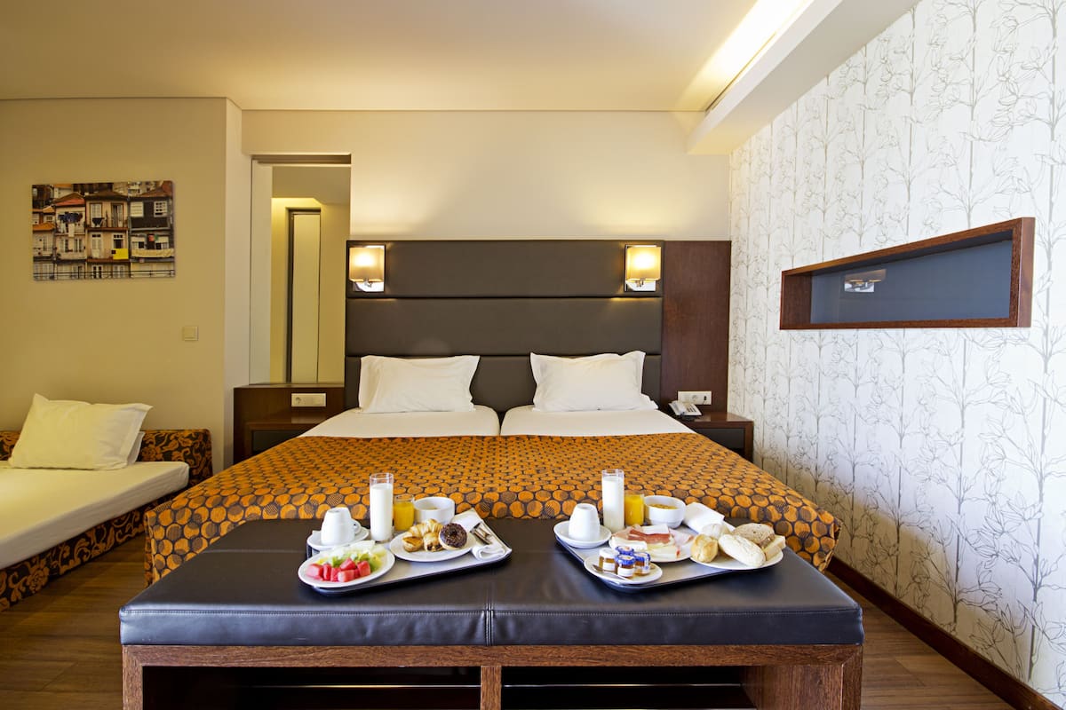 A hotel room with a large bed, two bedside tables, a small desk, and a breakfast tray with food and drinks.