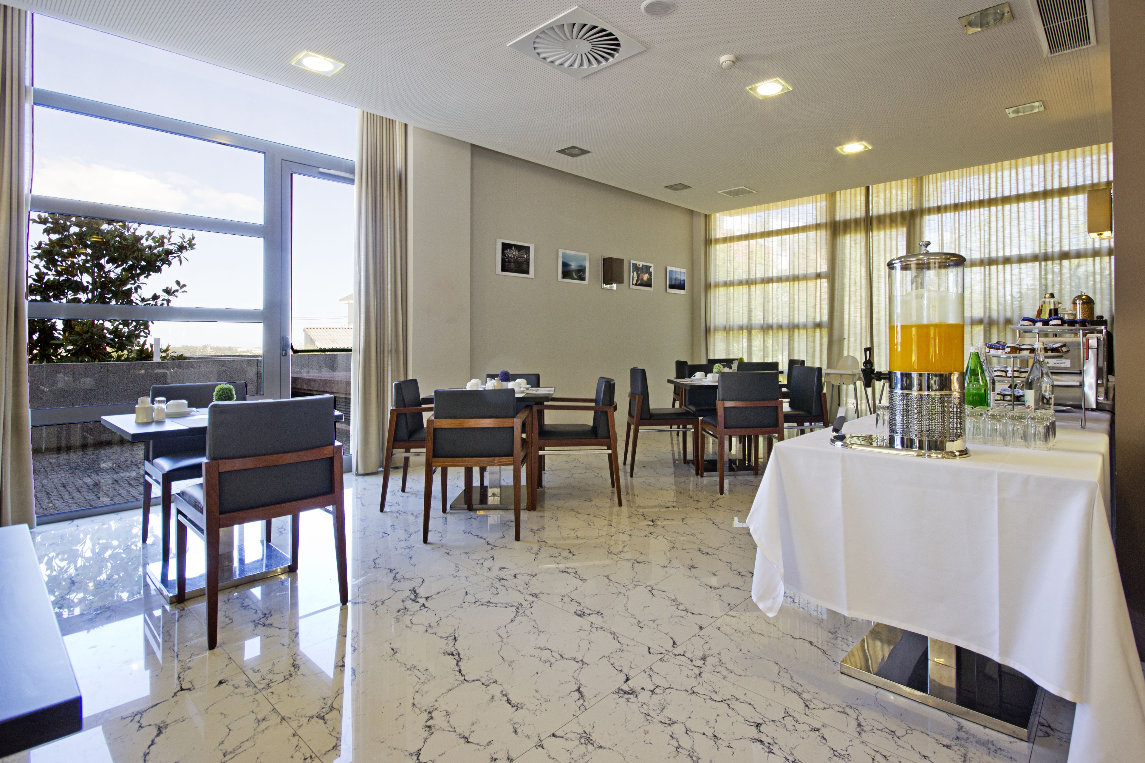 A modern dining area with marble flooring, multiple tables and chairs, and a buffet setup with a beverage dispenser.