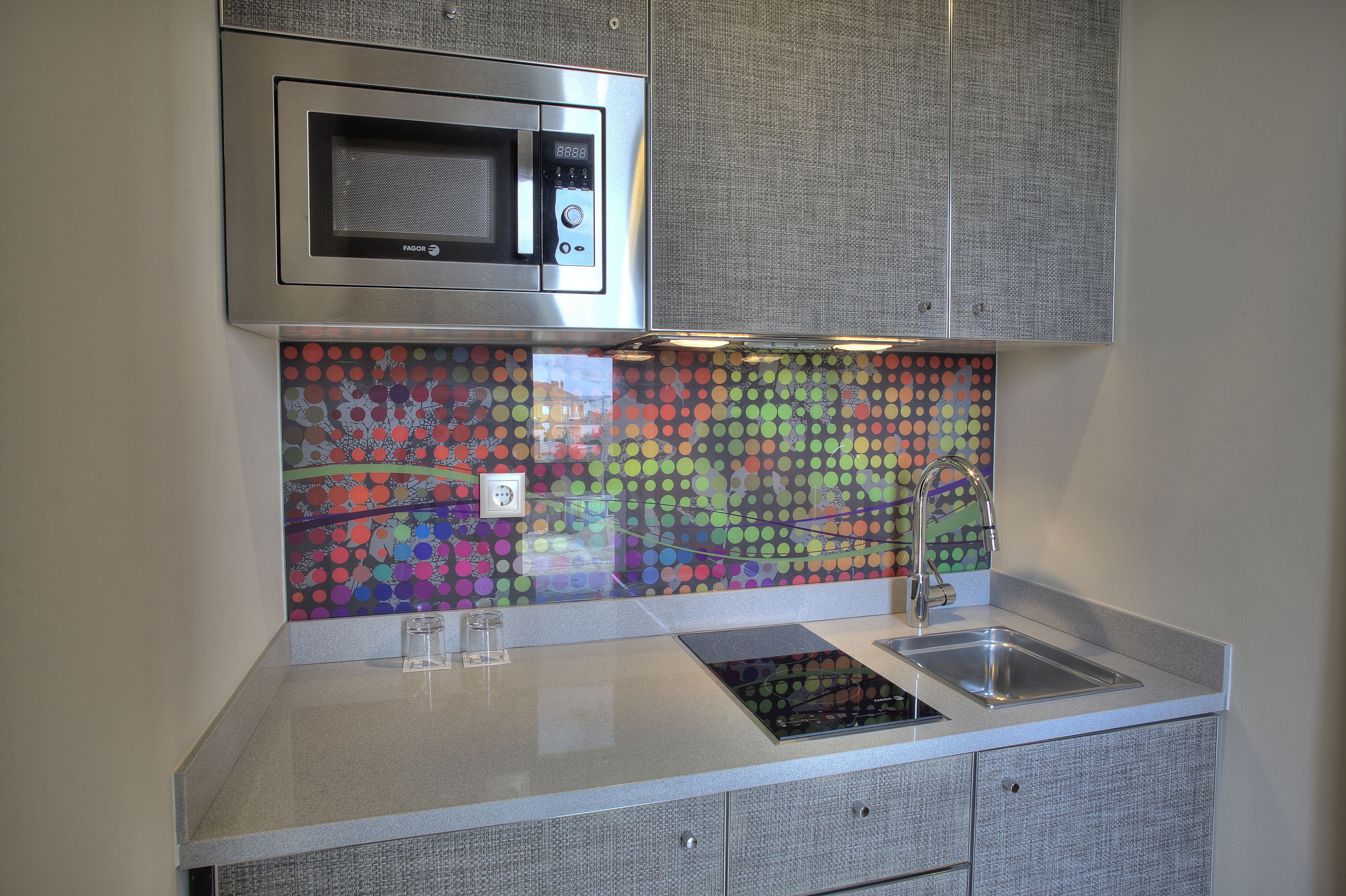 Uma cozinha com micro-ondas, painel de parede colorido, pia e fogão.