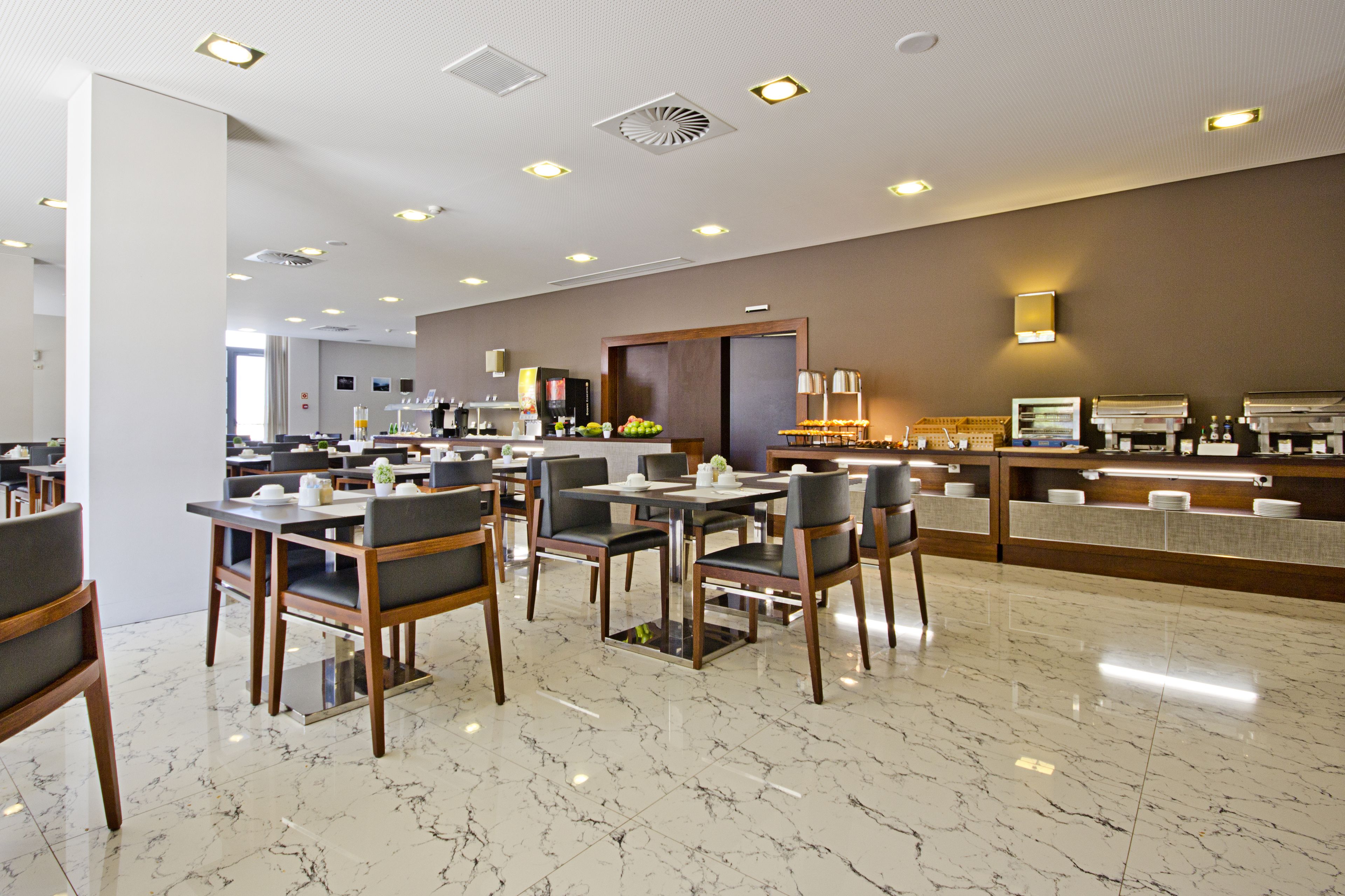 Um lobby de hotel moderno com piso de mármore, várias mesas de jantar com cadeiras, um balcão de recepção e um espelho grande.