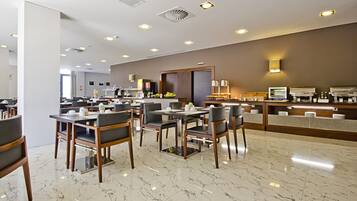 Um lobby de hotel moderno com piso de mármore, várias mesas de jantar com cadeiras, um balcão de recepção e um espelho grande.