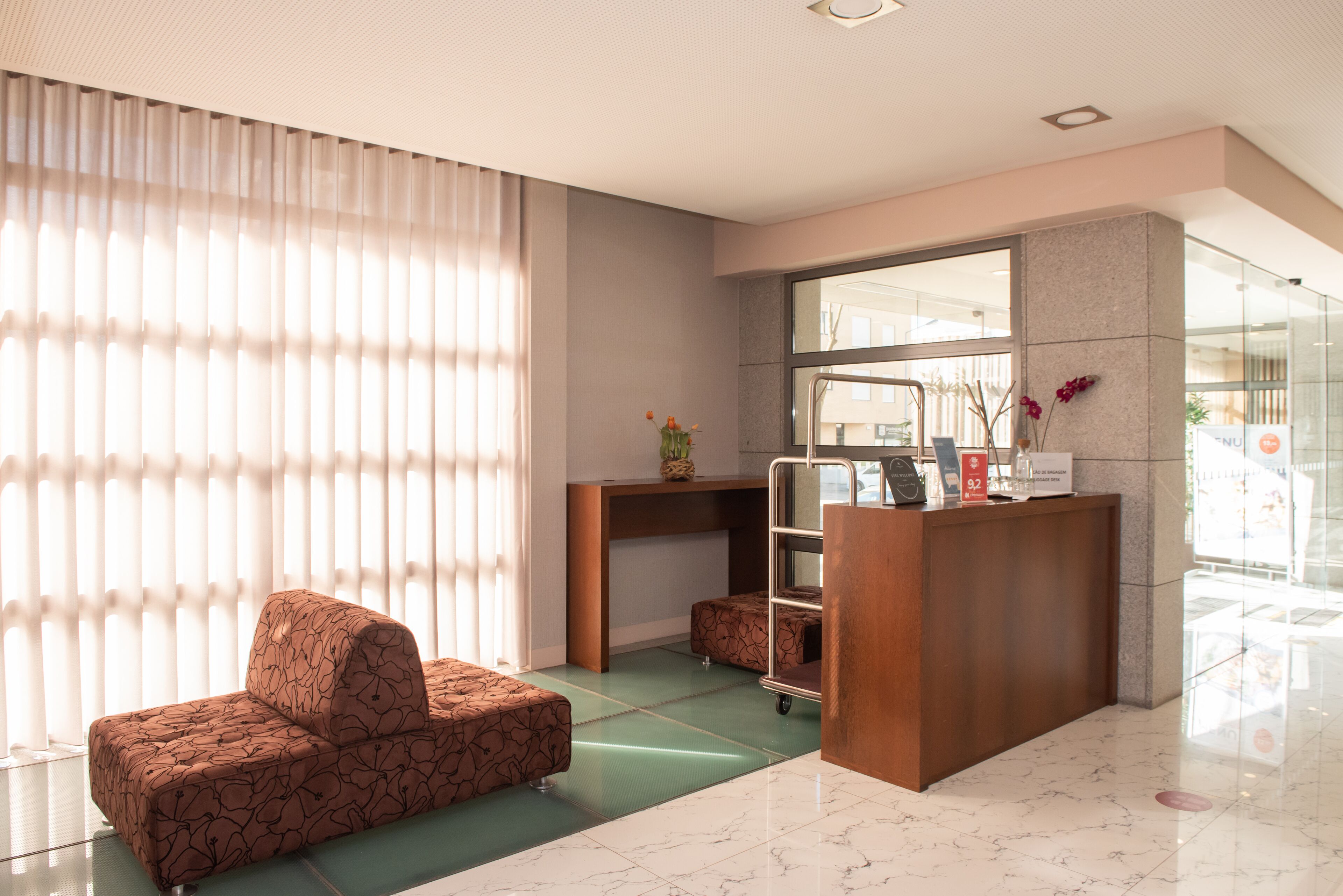 A reception area with a wooden desk, a cushioned seating area, and a large window with blinds.