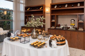 Una mesa de buffet con diversos pasteles y bebidas, rodeada de estanterías de madera con botellas de vino.