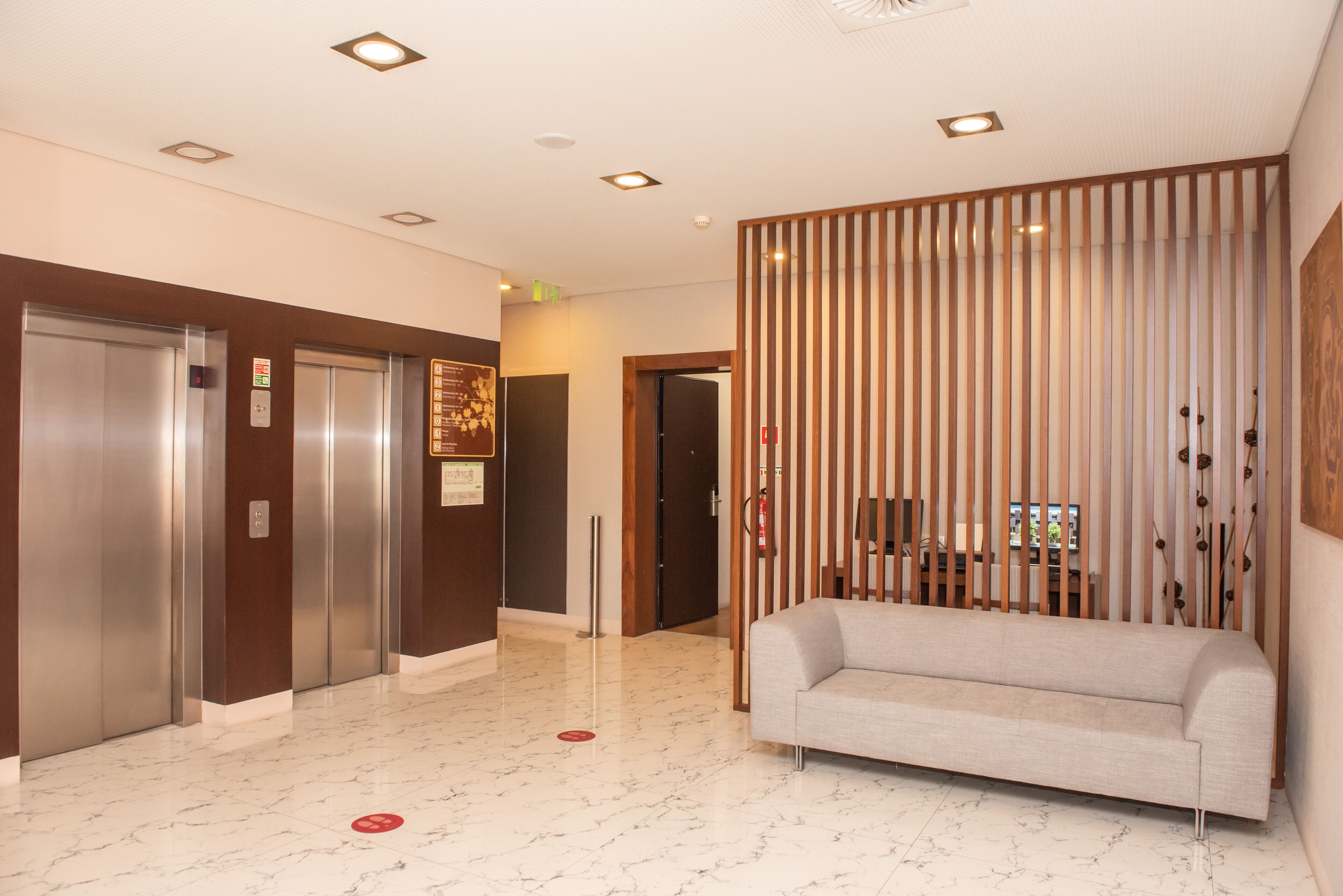 A hotel lobby with two elevators, a reception desk, a sofa, and a decorative wooden partition.