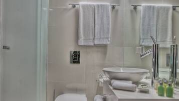 Ein modernes Badezimmer mit Duschkabine aus Glas, Toilette in Weiß, großem Waschbecken mit Spiegel und Handtuchhalter.
