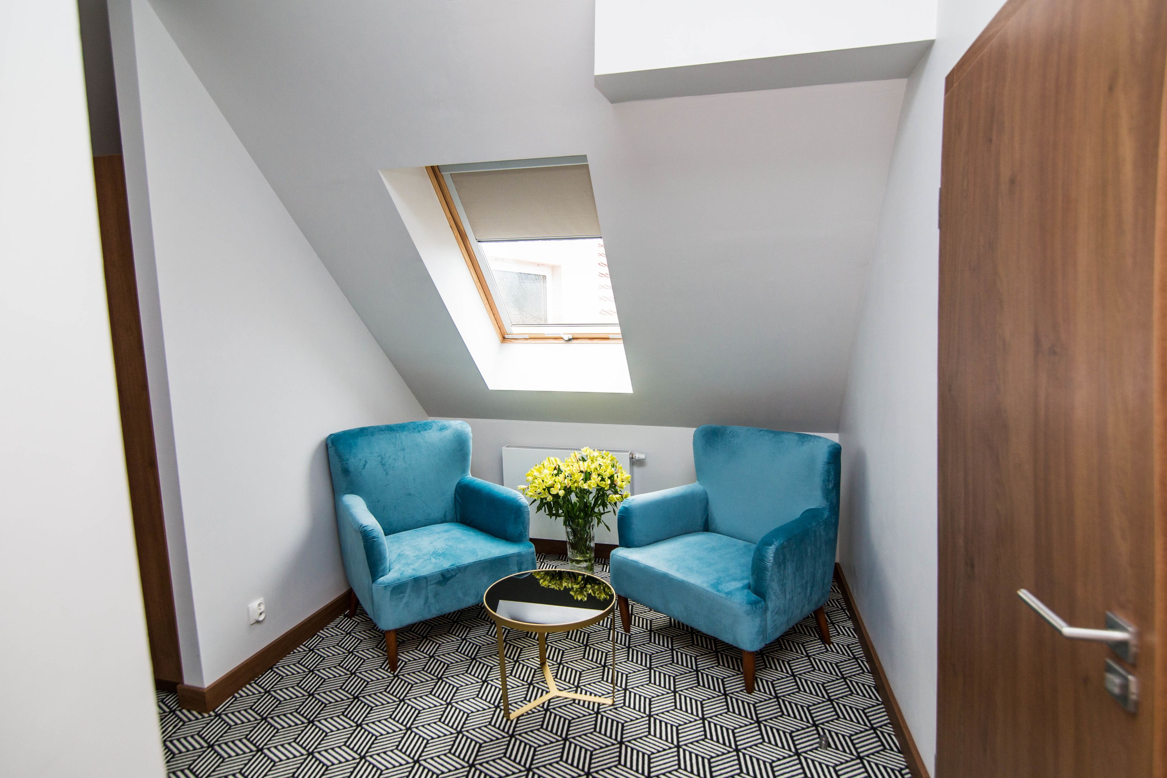 Una habitación pequeña y moderna con dos sillones azules, una mesita con un florero y un tragaluz.