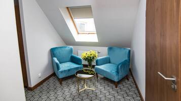 Una habitación pequeña y moderna con dos sillones azules, una mesita con un florero y un tragaluz.