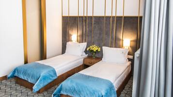 Een hotelkamer met twee eenpersoonsbedden, een nachtkastje met een lamp, een bloemenvaas en een vloer met een patroon.