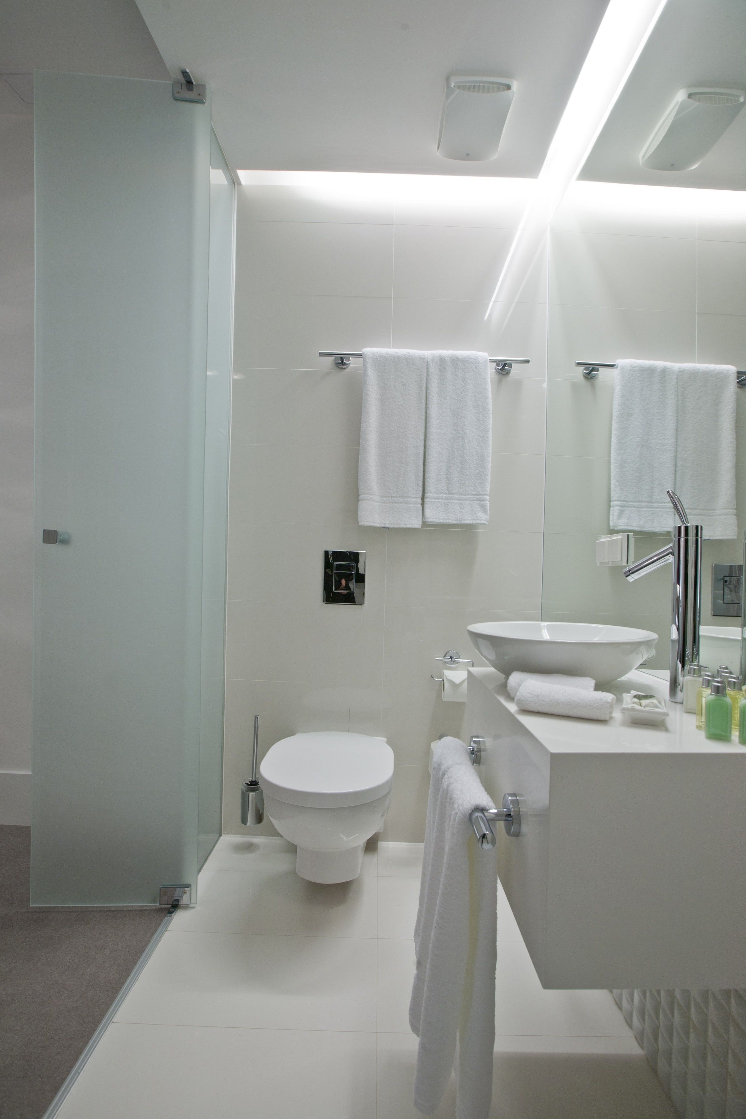 Ein modernes Badezimmer mit Duschkabine aus Glas, einer weißen Toilette, einem Waschbecken mit Spiegel und weißen Handtüchern.