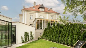 A modern house with a large garden, a glass door entrance, and a patio with a lounge chair.