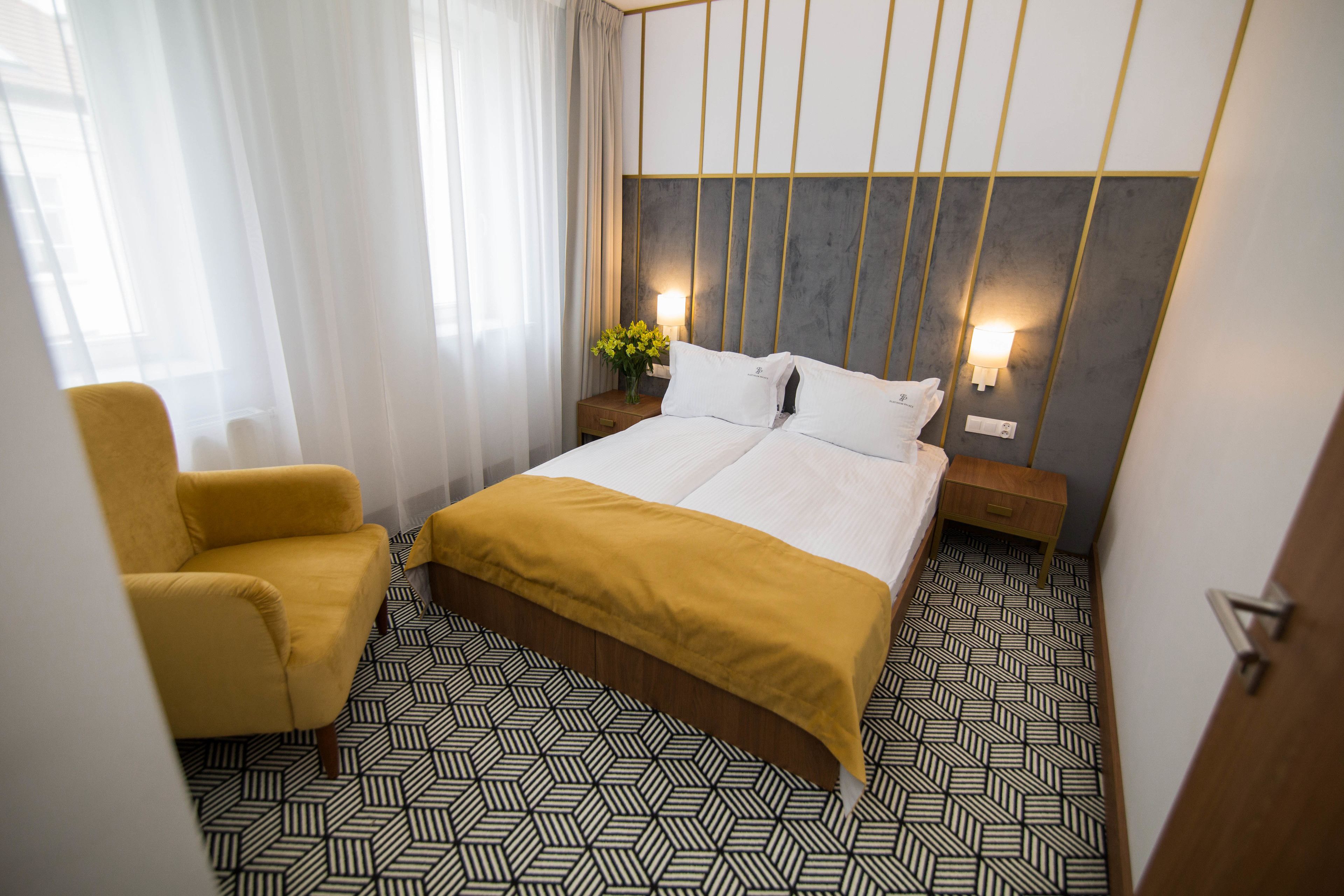 Une chambre d’hôtel avec un lit, une chaise, une table de chevet avec une lampe et un sol à motifs.