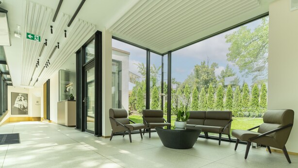 A modern lobby with a glass wall, a reception desk, and seating area with a potted plant.
