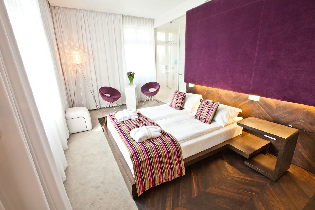 A modern hotel room with a large bed, a wooden nightstand, and a purple accent wall.