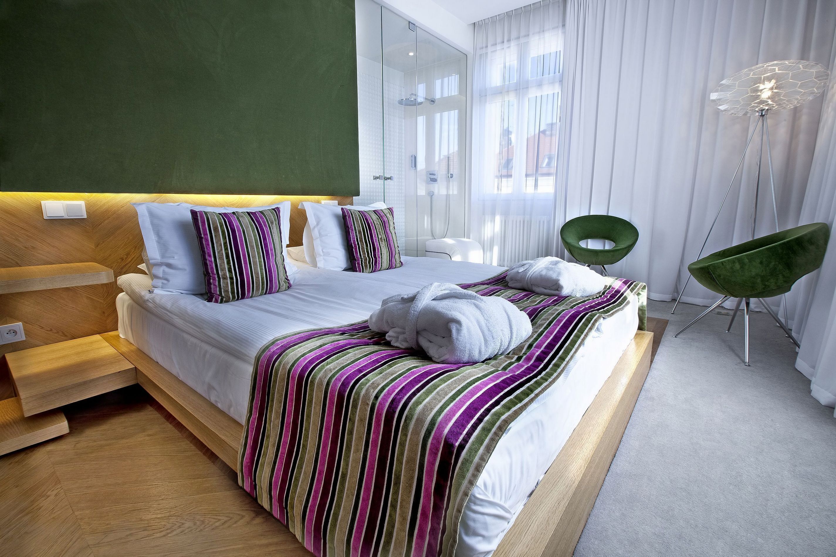 Ein modernes Hotelzimmer mit einem großen Bett, einer Dusche, einem grünen Sessel und einer Stehlampe.