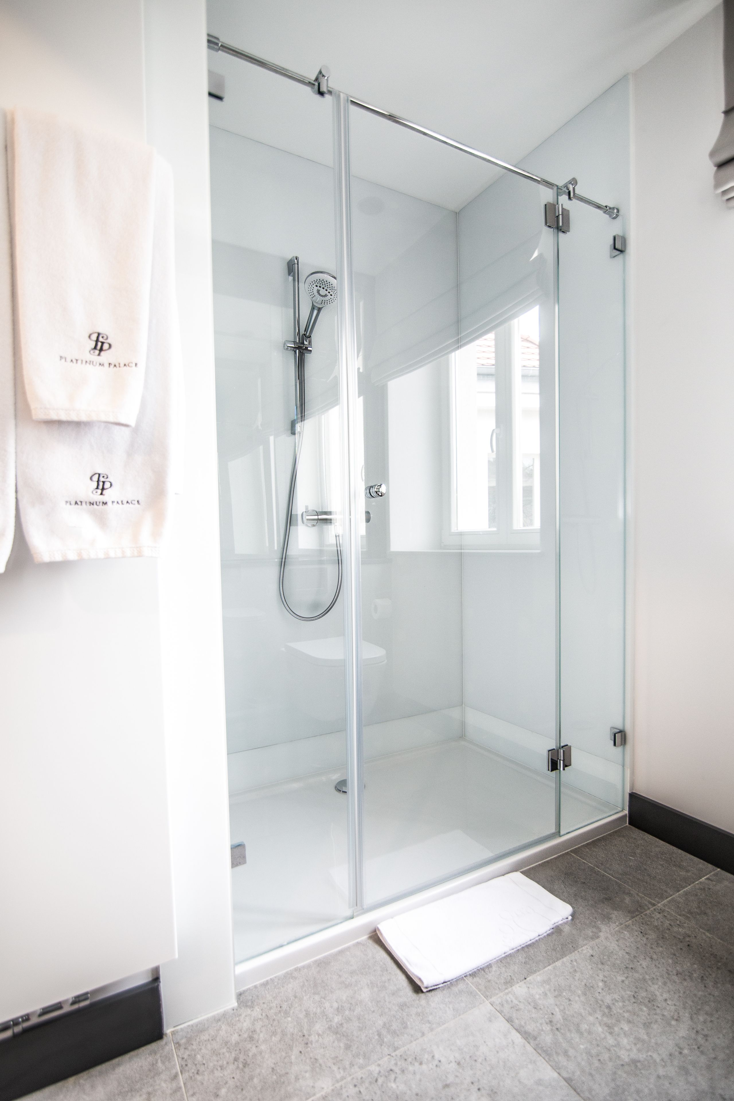 Une salle de bain moderne avec une douche à parois de verre, une serviette blanche accrochée au mur et un sol carrelé.