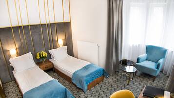 A hotel room with two beds, a small table, a chair, and a view of the outdoors.