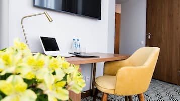 A modern hotel room with a desk, a flat-screen TV, a yellow armchair, and a patterned floor.