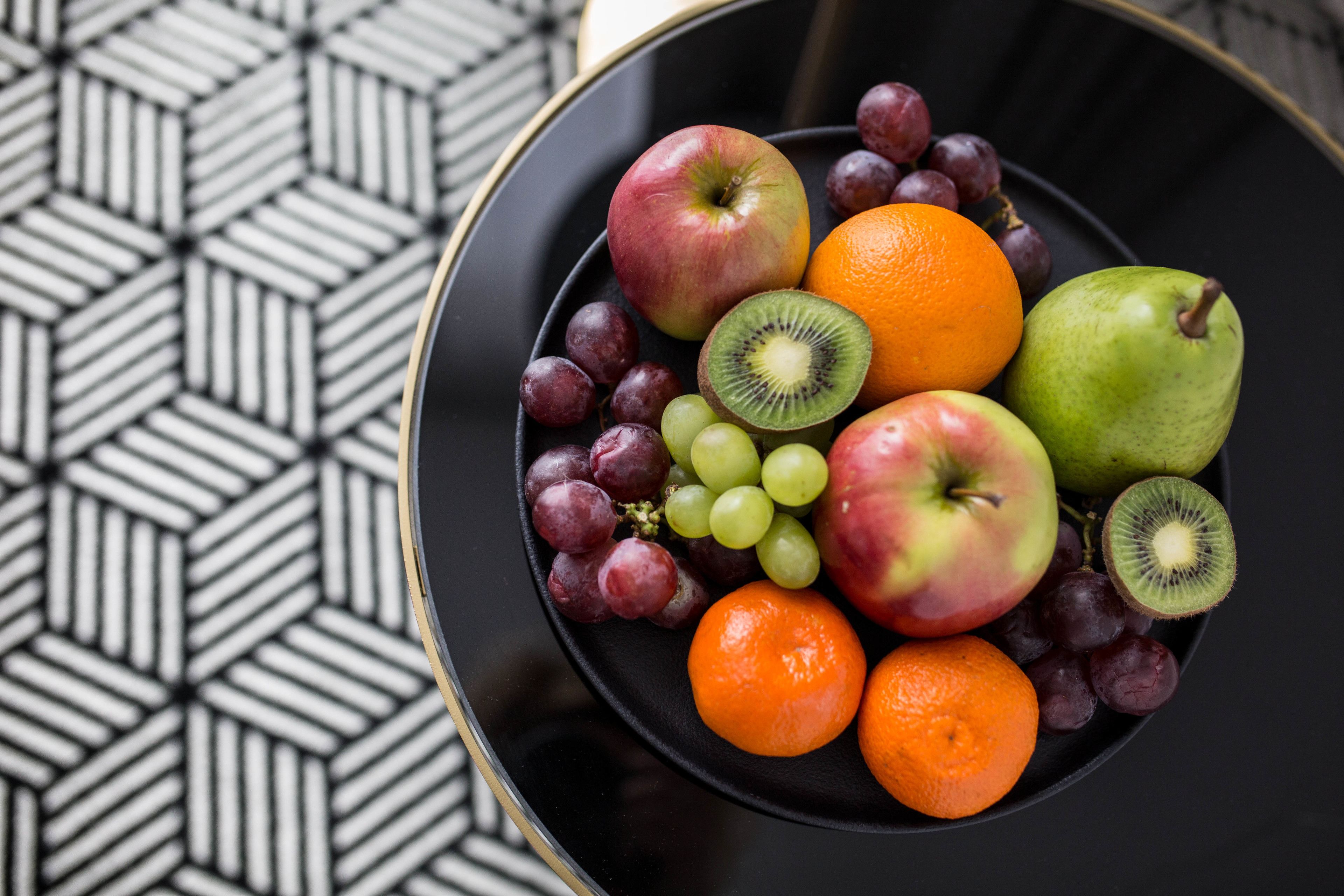 Eine Obstschale mit Äpfeln, Orangen, Trauben und Kiwis auf einer schwarzen Platte.