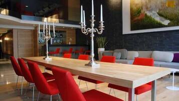 A modern dining area with a long wooden table, red chairs, and a candelabra centerpiece.