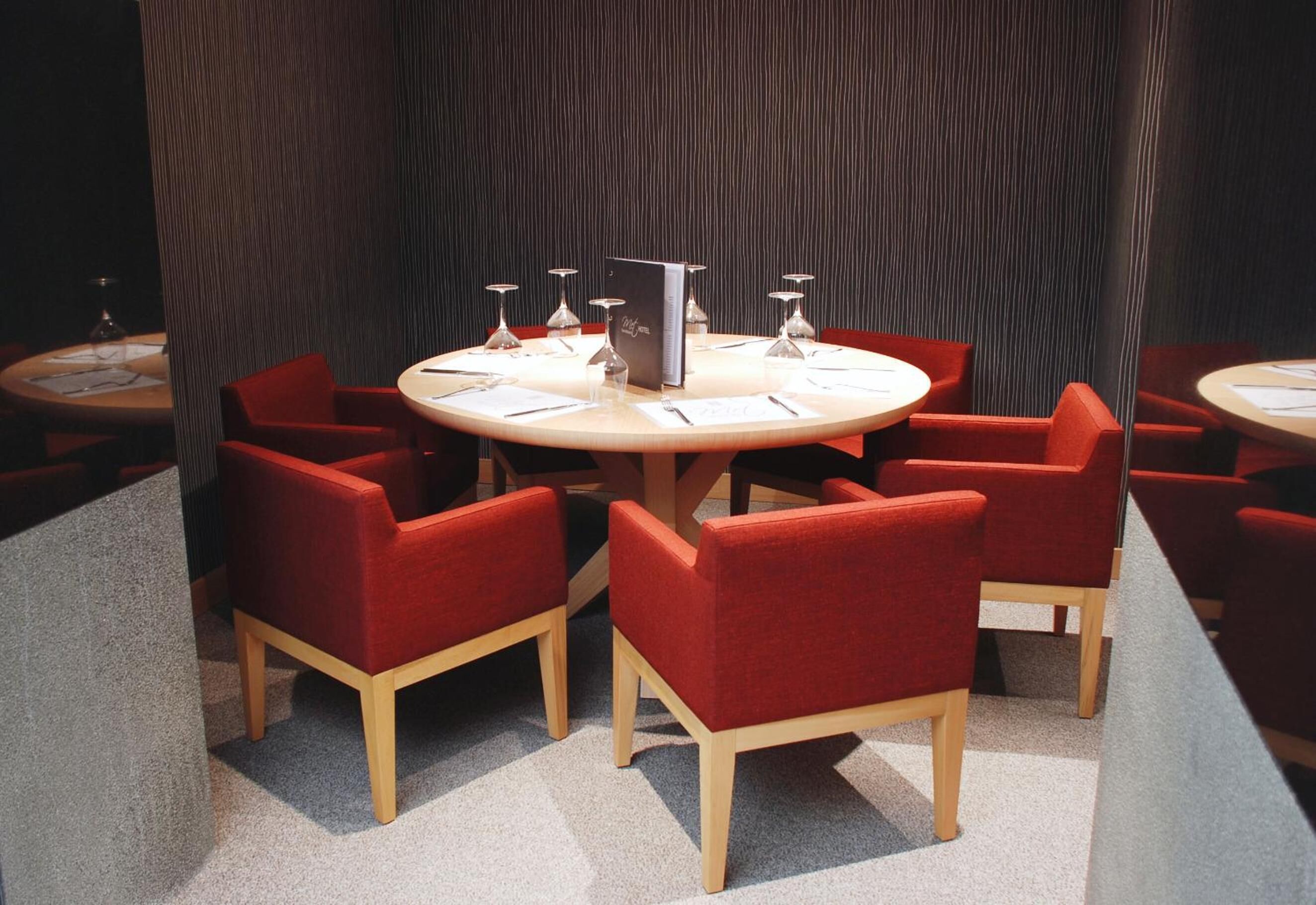 Un salón de conferencias con mesas redondas, sillas rojas y una pared oscura con textura.