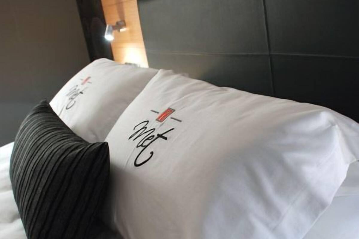 A neatly made bed with white linens and a black pillow, a wooden headboard, and a wall with a circular pattern.