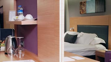 A hotel room with a wooden desk, a bed with a headboard, a nightstand, and a purple wall.