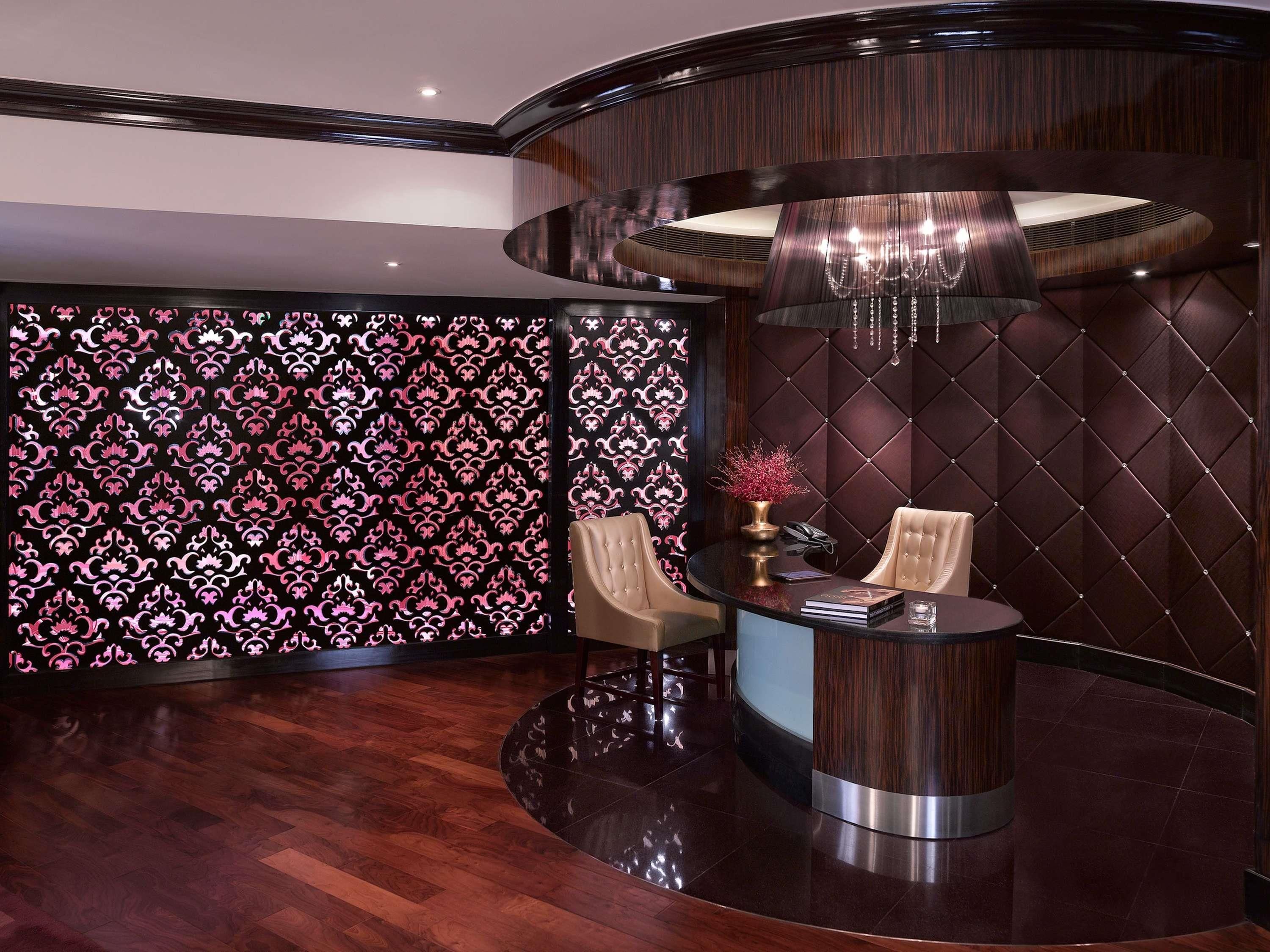 A luxurious room with a round desk, two chairs, a decorative vase, and a patterned wallpaper.