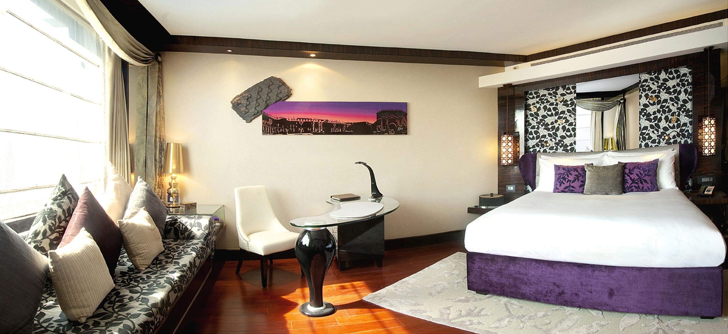 Een moderne hotelkamer met een groot bed, een slaapbank, een klein tafeltje en een stadsgezichtschilderij aan de muur.