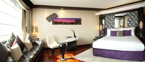 Een moderne hotelkamer met een groot bed, een slaapbank, een klein tafeltje en een stadsgezichtschilderij aan de muur.