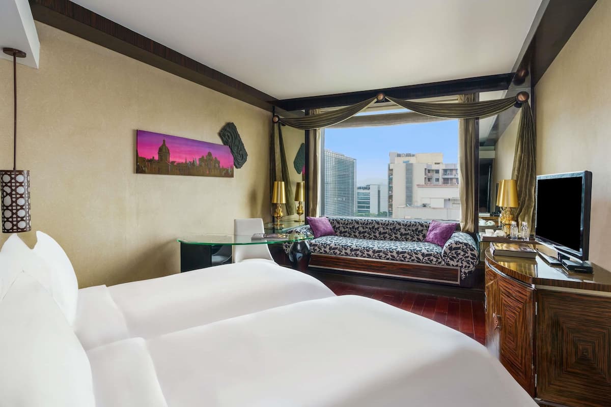 A hotel room with a large bed, a sofa, a desk, a TV, and a city view.