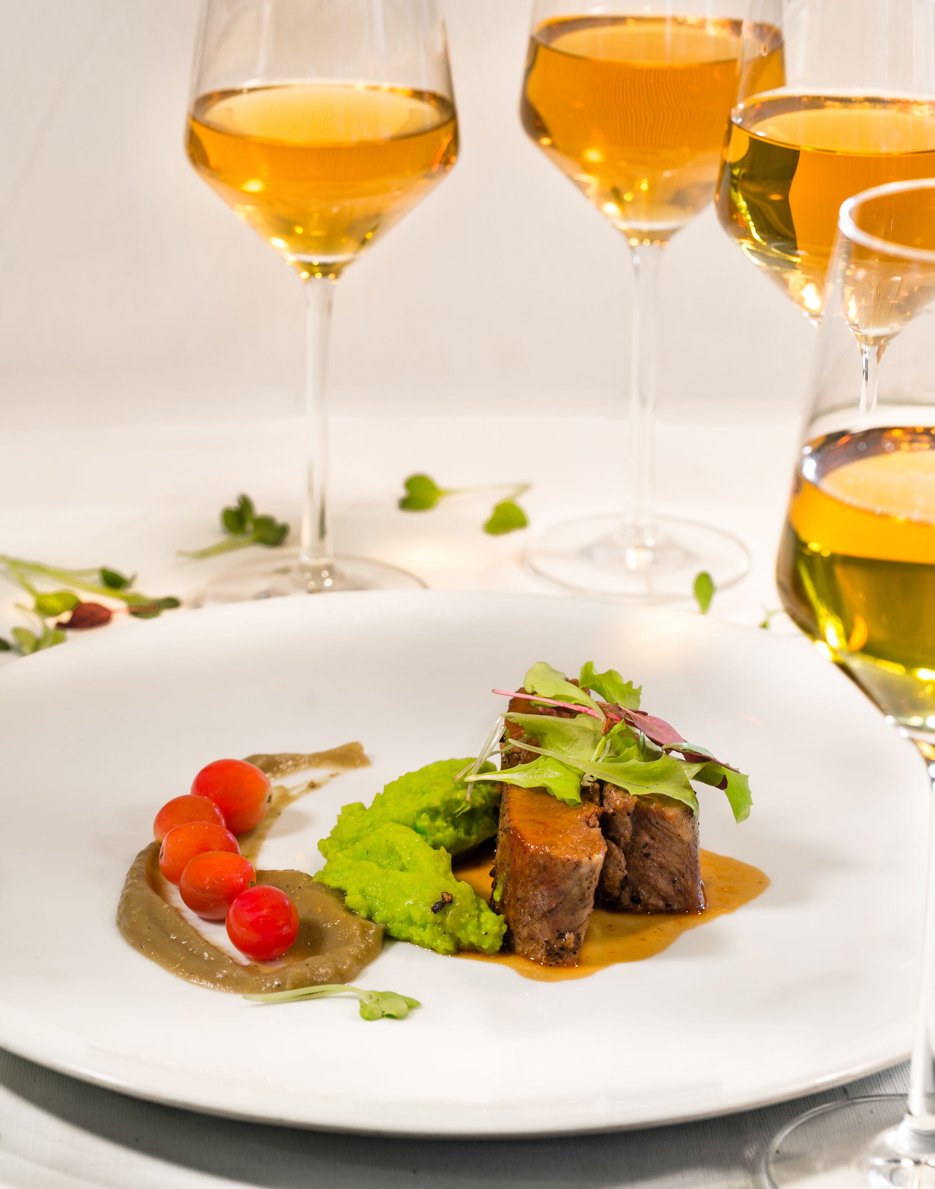 Une assiette blanche contenant un plat de viande, une garniture verte et des baies rouges.