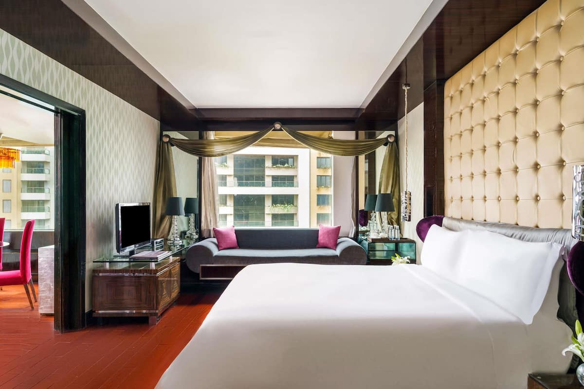 A hotel room with a large bed, a desk, a sofa, and a view of buildings through the window.