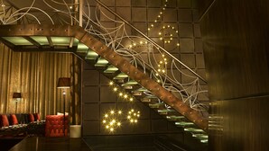 A modern interior with a wooden staircase, a seating area with red chairs, and a patterned wall. - Sofitel Mumbai BKC Hotel (Mumbai)