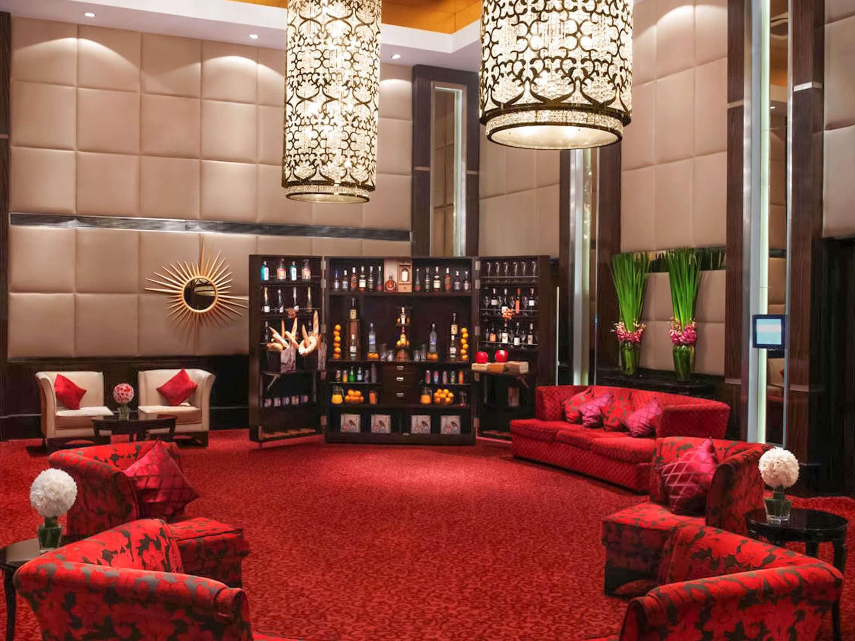 A lobby with red upholstered sofas, a bar area with liquor bottles, and decorative lighting fixtures.