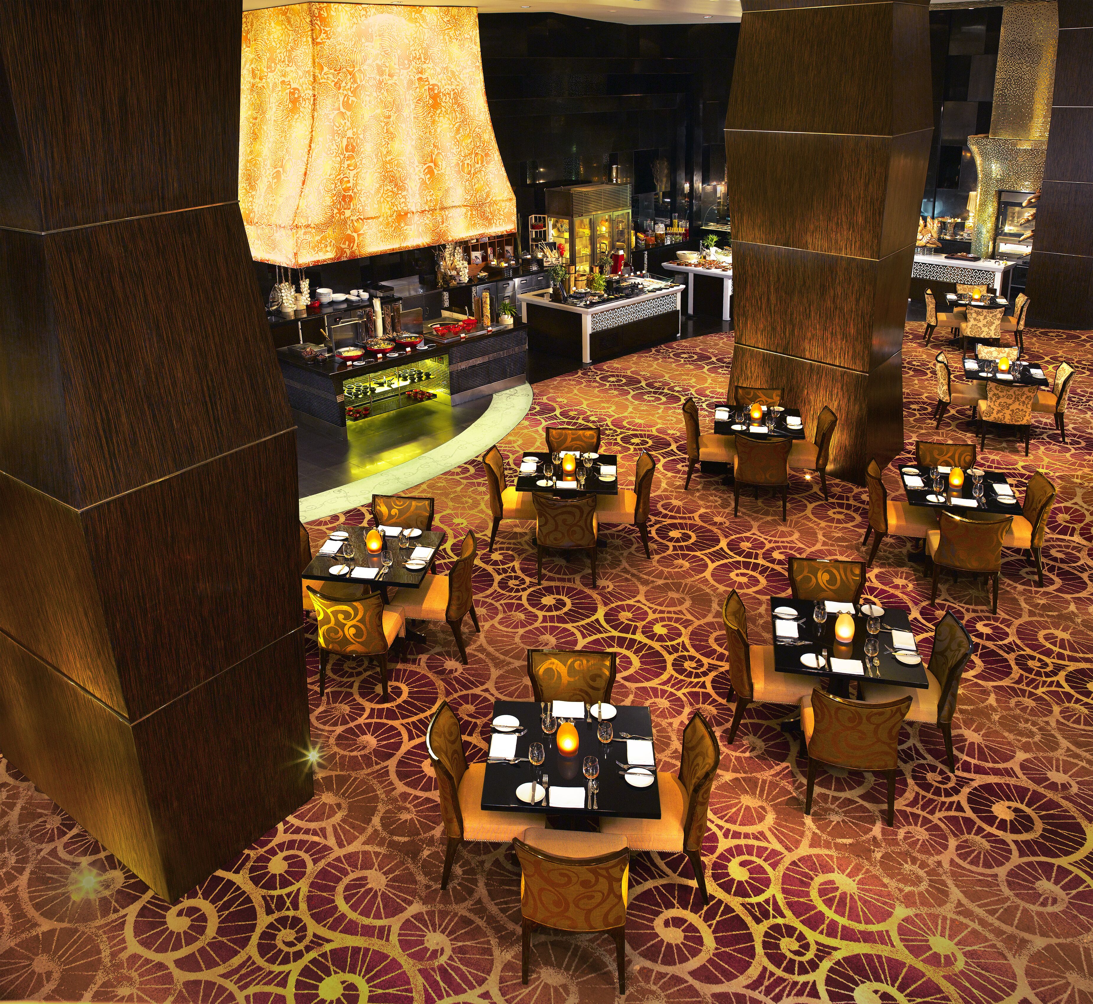 A restaurant with multiple tables and chairs, a bar area, and a patterned carpet.