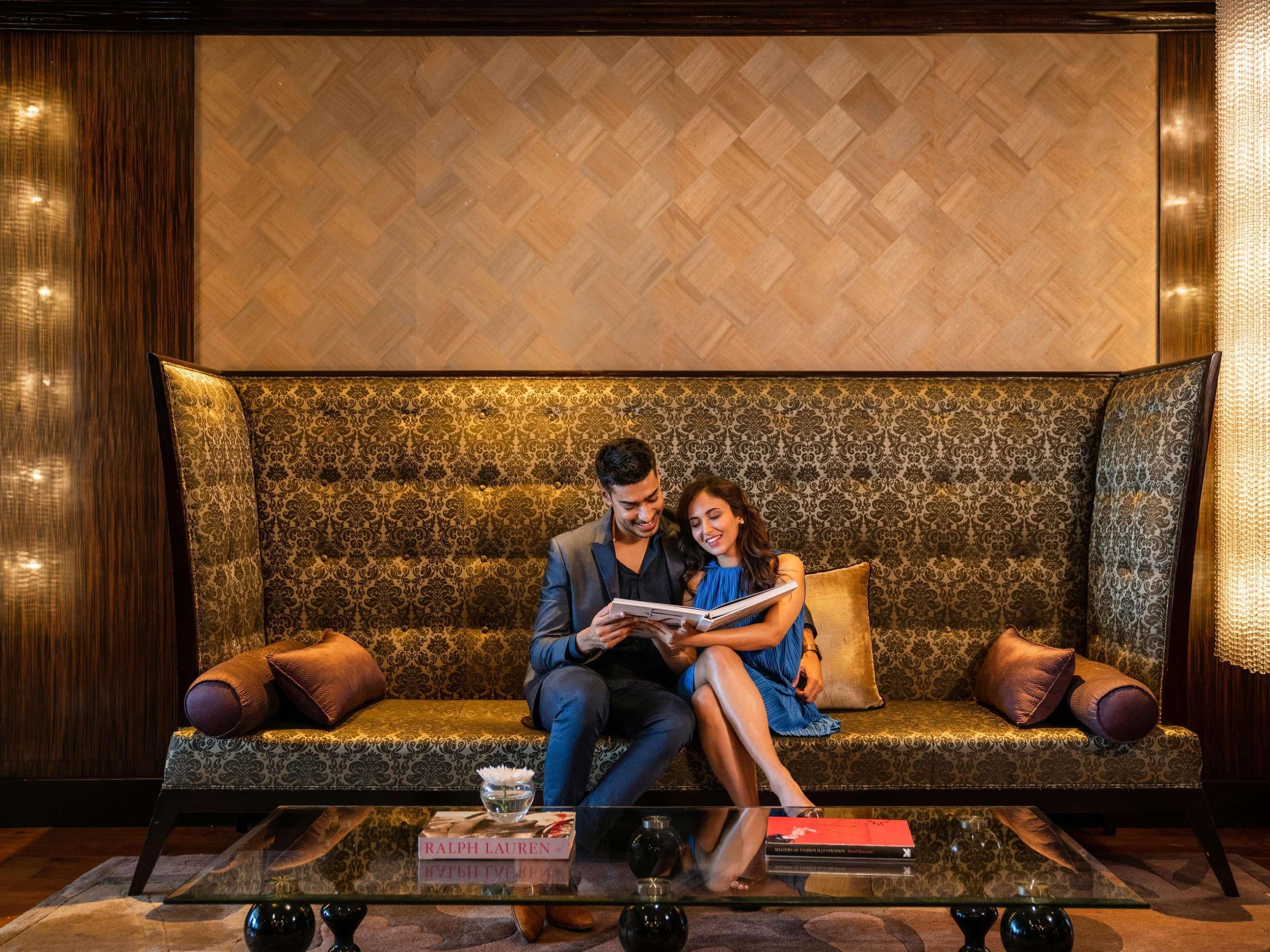 A couple sitting on a patterned sofa with a glass coffee table in front.