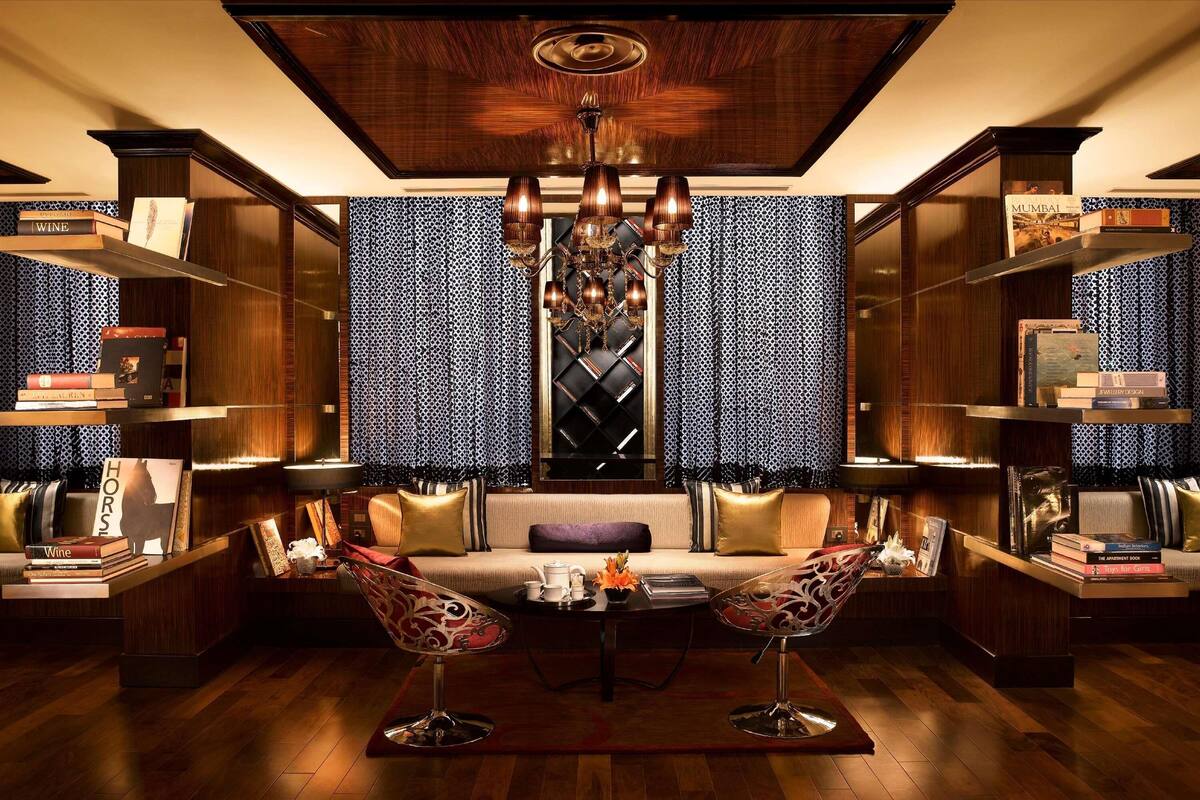 A library with bookshelves, a sofa, two chairs, a chandelier, and patterned curtains.