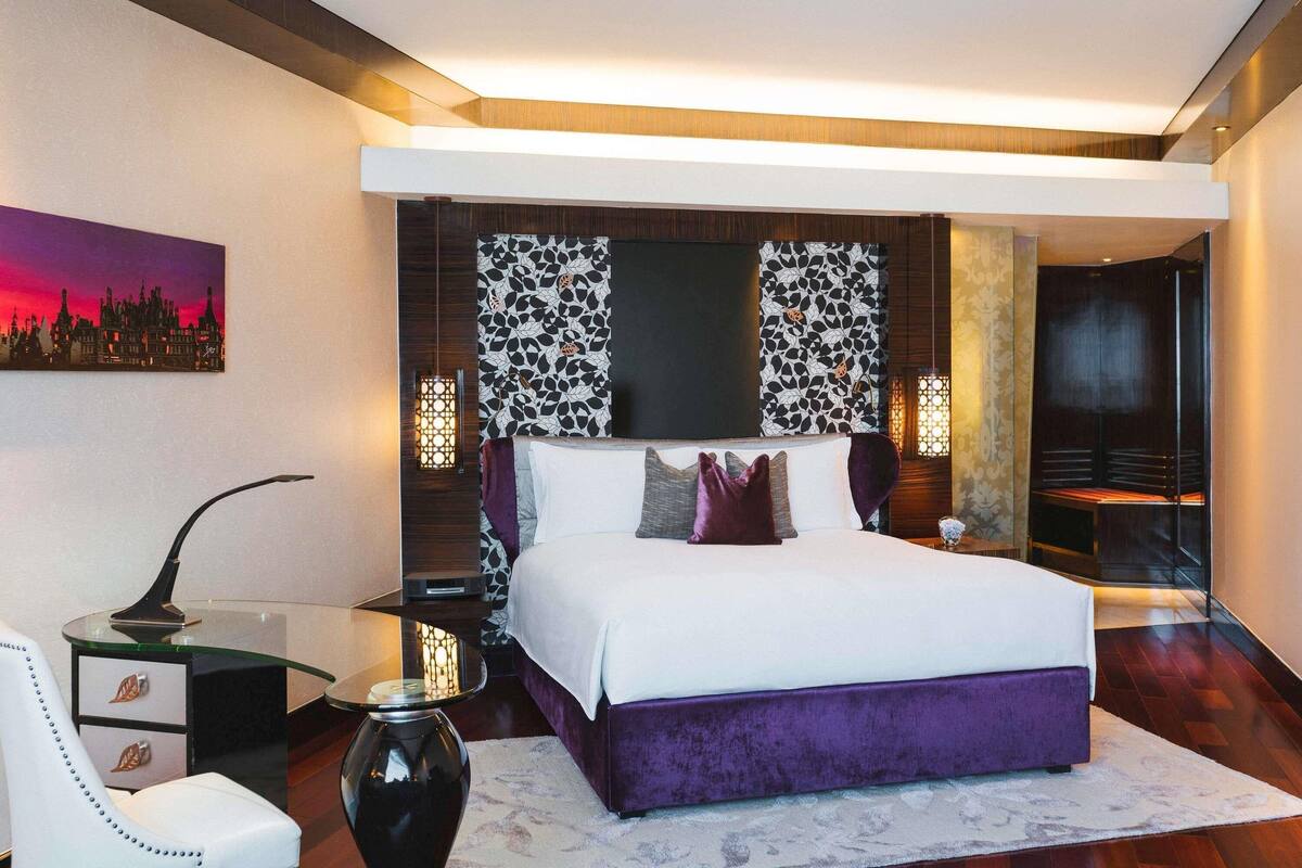 A modern hotel room with a large bed, a desk, and a chair.