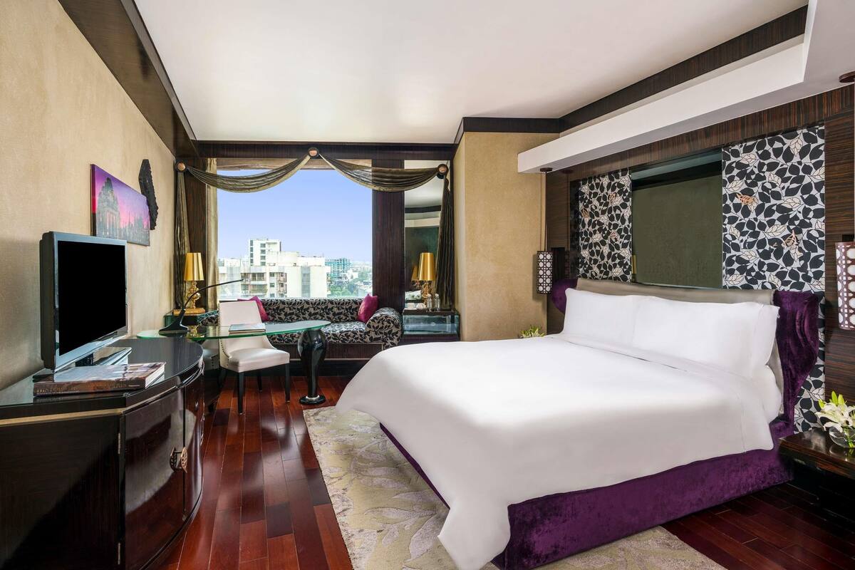 A hotel room with a large bed, a desk with a computer, a TV, and a view of the city.