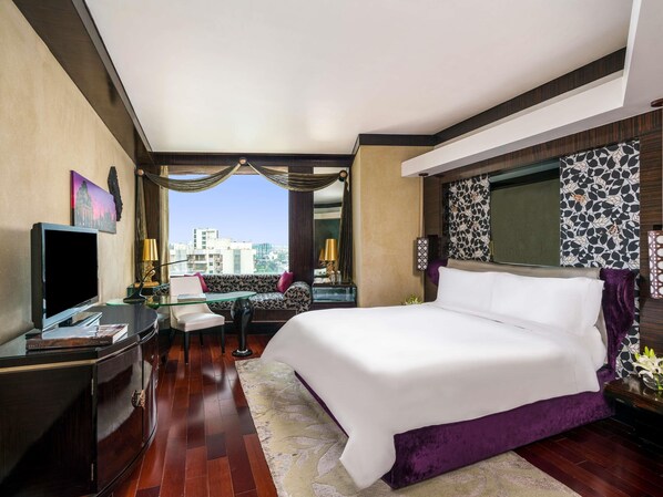 A hotel room with a large bed, a desk with a computer, a TV, and a view of the city.