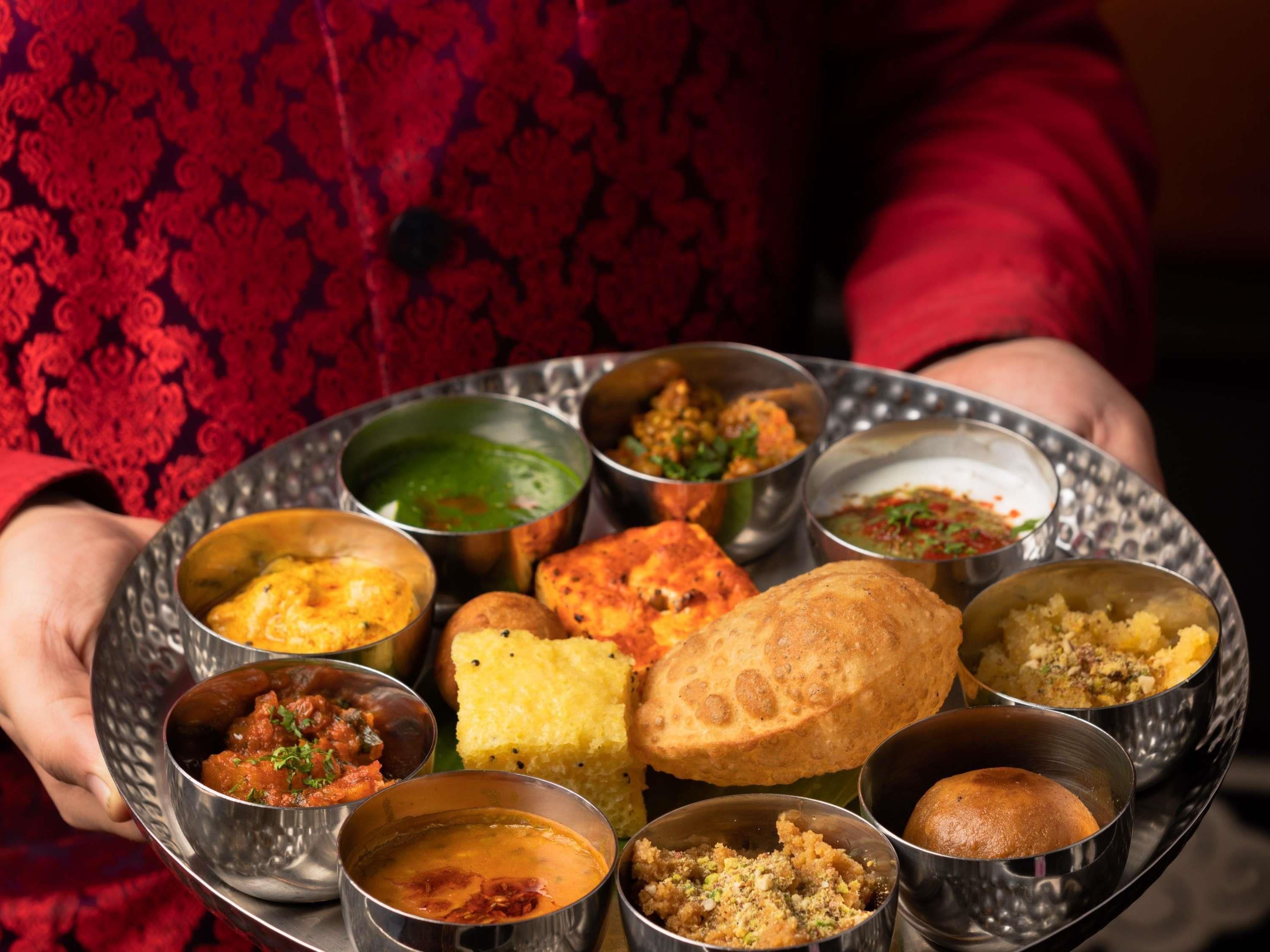 A person holding a tray with various Indian dishes and sauces.
