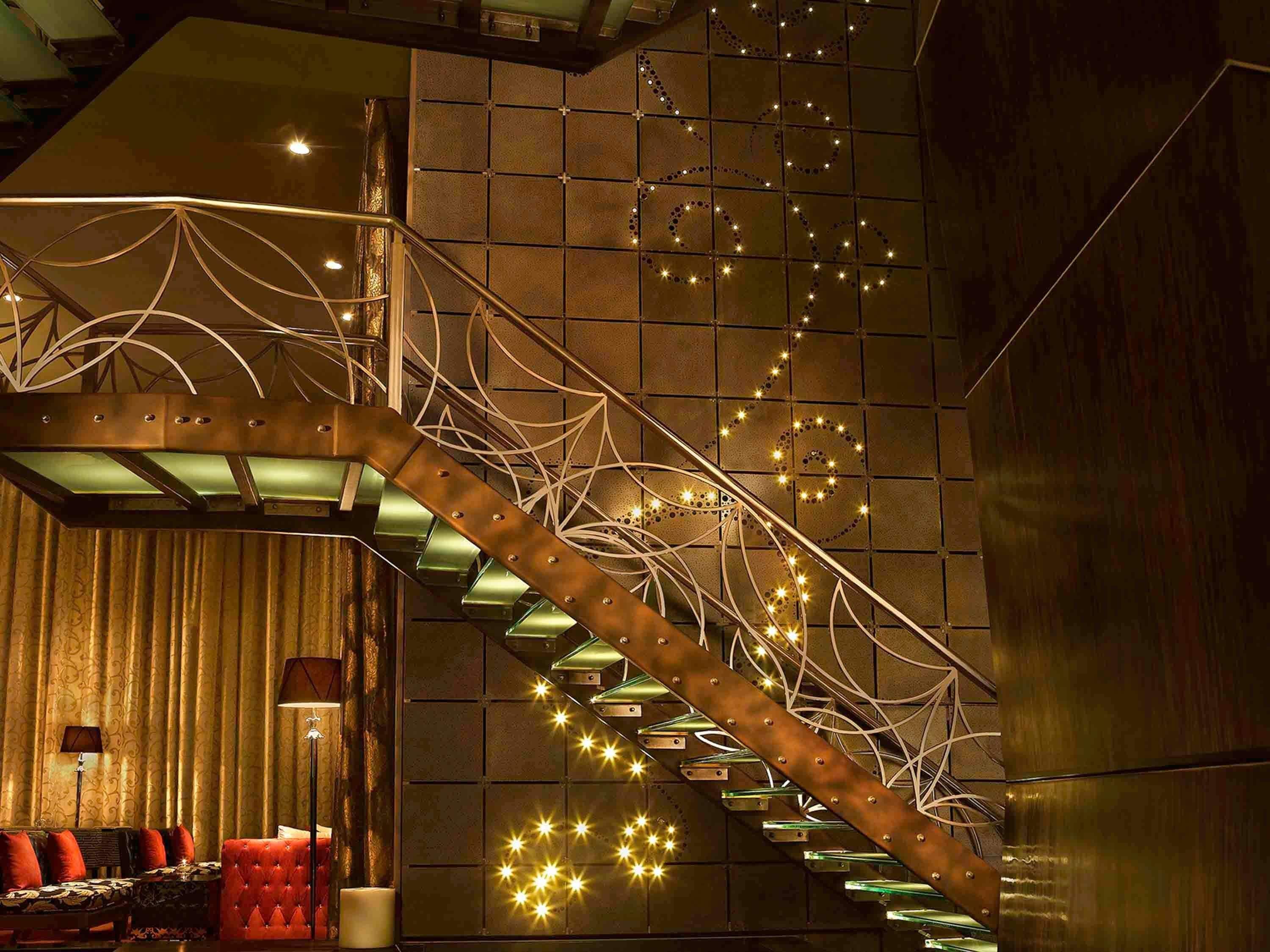 Un escalier doté d’une rampe en métal et de luminaires en forme d’étoile, menant à une pièce dont le mur est orné de motifs et qui contient un canapé rouge.